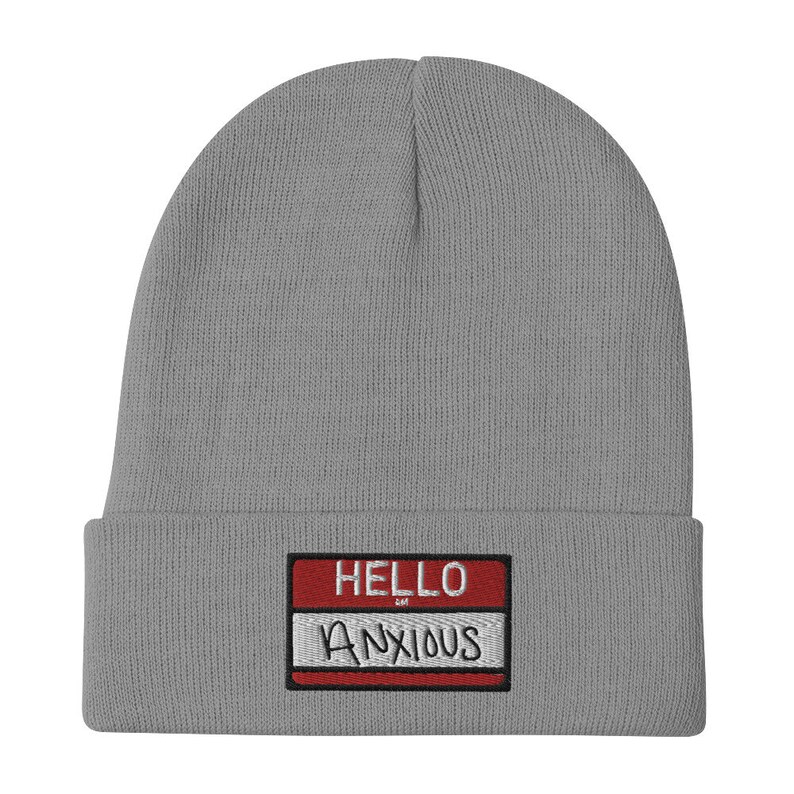 May include: Gray knitted beanie with a red and white name tag that reads "HELLO ANXIOUS".