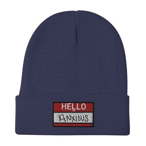May include: A navy blue beanie with a red and white name tag that says "HELLO ANXIOUS" in white embroidery.