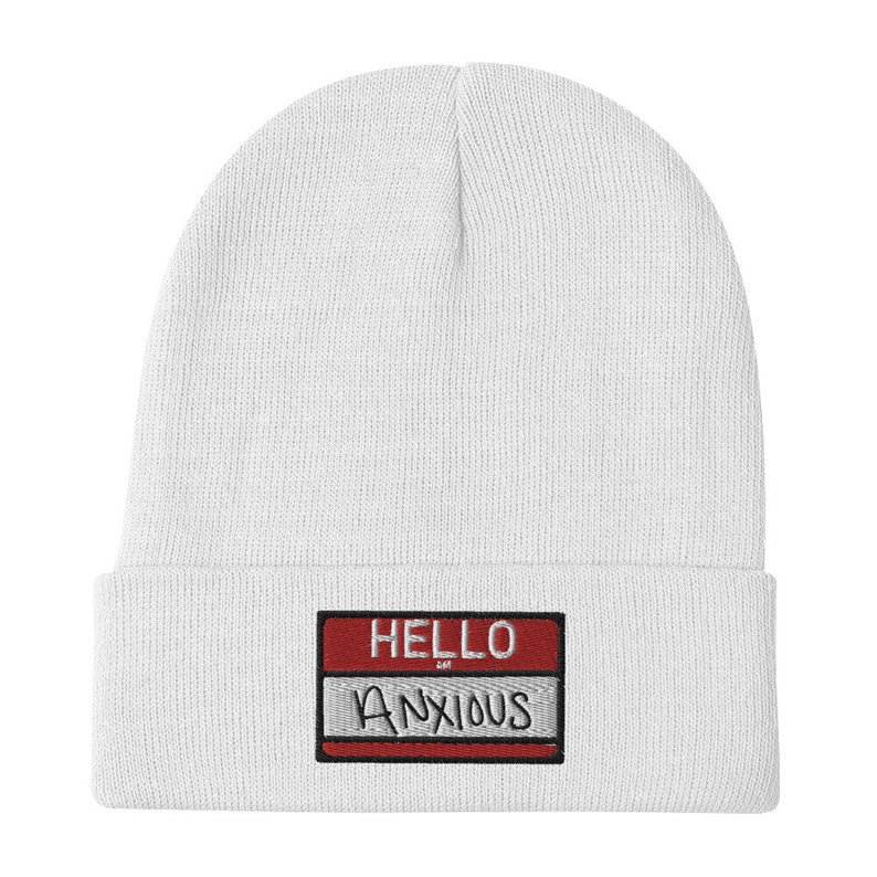 May include: White knit beanie with a red and gray name tag that says "HELLO ANXIOUS" in black embroidery.