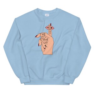 May include: Light blue sweatshirt with a graphic of a hand with a finger over its mouth, with the text "SHUT THE FUCK UP." printed on the finger.