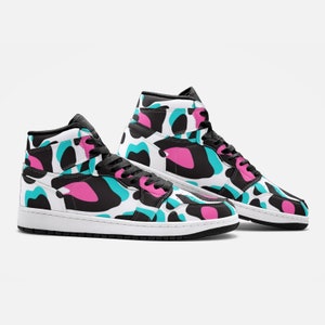 May include: High-top sneakers with a white base and a colorful pattern of black, teal, and pink shapes. The shoes have black laces, a black collar, and a white sole. The design is repeated on both shoes.