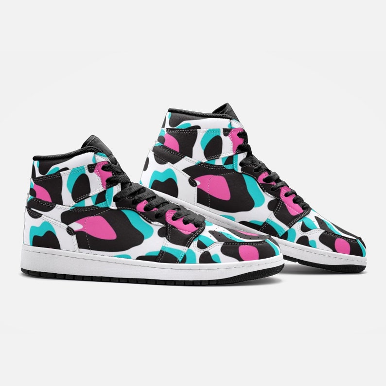 May include: High-top sneakers with a white base and a colorful pattern of black, teal, and pink shapes. The shoes have black laces, a black collar, and a white sole. The design is repeated on both shoes.