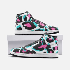 May include: High-top sneakers with a white base and a colorful pattern of black, pink, and teal shapes. The shoes have black laces, a black sole, and a white midsole. The sneakers are displayed on a white box.