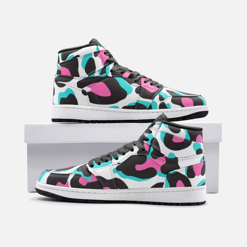 May include: High-top sneakers with a white base and a colorful pattern of black, pink, and teal shapes. The shoes have black laces, a black sole, and a white midsole. The sneakers are displayed on a white box.