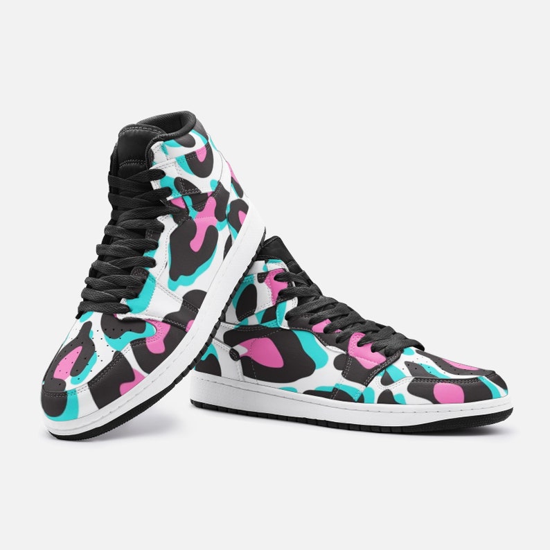 May include: High-top sneakers with a vibrant pattern. The shoes feature a white base with a colorful design of black, pink, and teal shapes. They have black laces, a black collar, and a white sole. The sneakers are designed for casual wear.