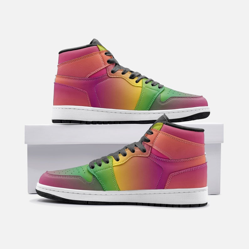 May include: High-top sneakers with a vibrant rainbow gradient design. The shoes feature a white sole, black laces, and a padded collar. The color transitions from pink to orange, yellow, and green. The sneakers are displayed on a white surface.
