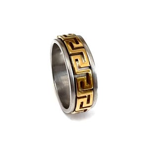 May include: A two-tone ring with a gold Greek key design on a silver band. The ring is a classic style, suitable for everyday wear. The gold detailing provides a striking contrast against the silver.