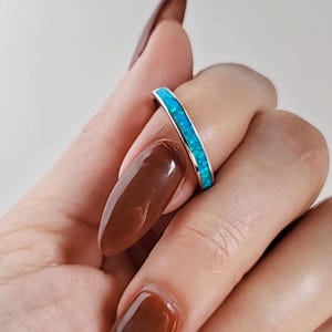 May include: A thin silver band ring with a row of turquoise blue opal stones set around the entire band.