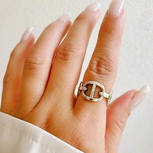 Puede incluir: Un anillo de plata con un diseño de cadena de eslabones que presenta una forma de 'H' entrelazada repetida.