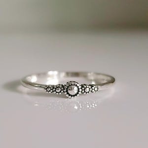 May include: A silver ring with a textured band and a small, round, raised center piece.