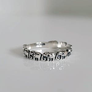 May include: A silver ring with a continuous design of small elephant figures.