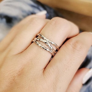 May include: A set of three silver rings with a twisted, textured design. The rings are stacked on a finger.