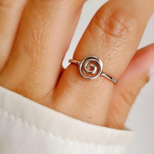 May include: A silver ring with a spiral design. The ring is on a finger.