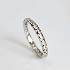 May include: A silver ring with a repeating diamond-shaped openwork design. The ring is thin and appears to be made of a shiny metal. The ring is set against a white background.