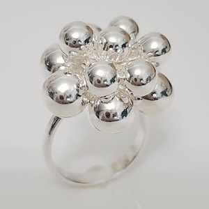 May include: A silver ring featuring a cluster of polished, spherical beads forming a floral-like design. The ring's band is a simple, smooth silver. The overall design is modern and eye-catching, suitable for everyday wear or special occasions.