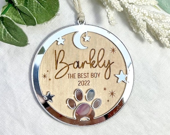 May include: A silver and wood Christmas ornament with a paw print, stars, and a crescent moon. The ornament is personalized with the name "Barkly" and the text "The Best Boy 2022".