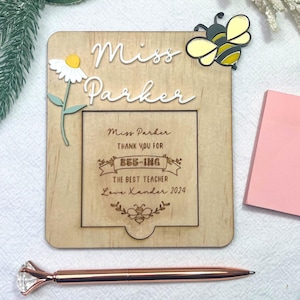 May include: Wooden sign with the text "Miss Parker" and a message thanking the teacher for "bee-ing" the best teacher. The sign has a small cutout for a photo or note. There is a yellow and black bee sticker on the sign.