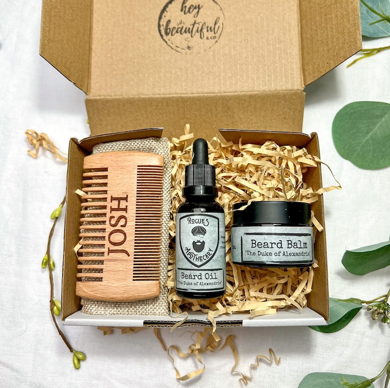 K&ouml;nnte beinhalten: Eine Geschenkbox gef&uuml;llt mit Bartpflegeprodukten. Die Box enth&auml;lt einen Holzkamm mit dem eingravierten Namen "JOSH", eine Flasche Bart&ouml;l mit der Aufschrift "ROGUES APOTHECARY Beard Oil The Duke of Alexandria" und ein Glas Bartbalsam mit der Aufschrift "Beard Balm The Duke of Alexandria".