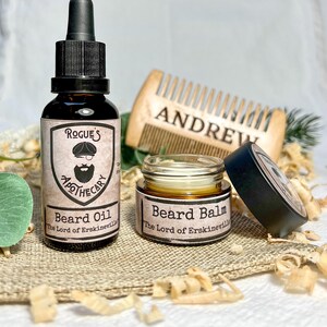 K&ouml;nnte beinhalten: Zwei Bartpflegeprodukte, eine Glasflasche mit Bart&ouml;l und ein Glastiegel mit Bartbalsam, beide mit schwarzen Etiketten und dem Text "Rogue's Apothecary" und "The Lord of Erskineville". Die Produkte befinden sich auf einer Jutesurface mit Holzsp&auml;nen.