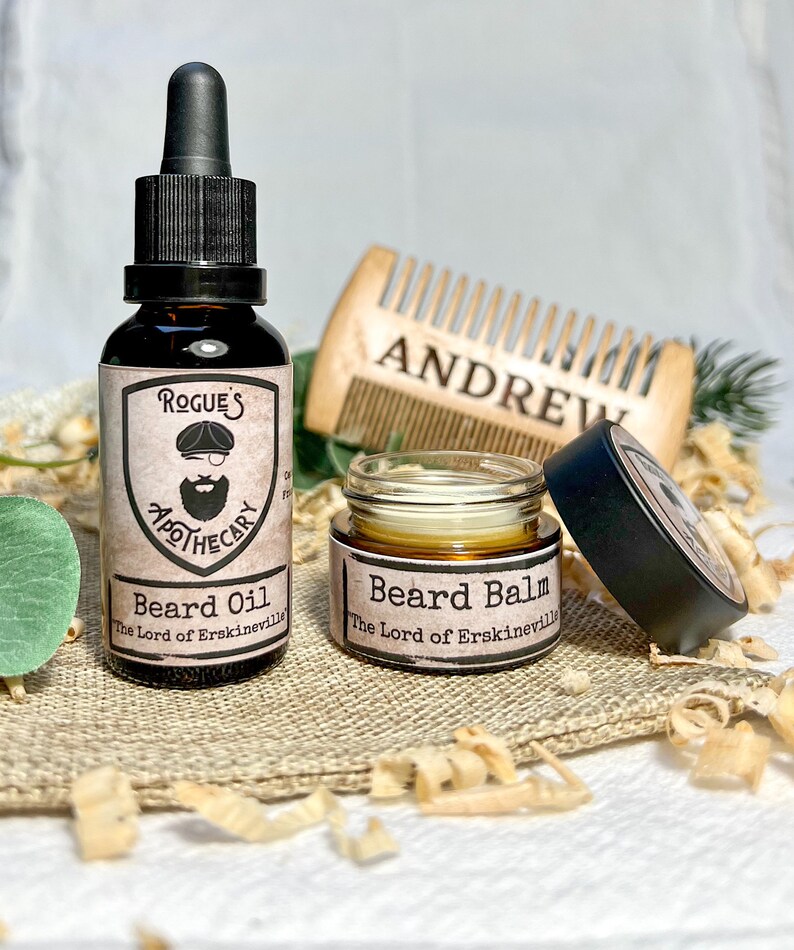 K&ouml;nnte beinhalten: Zwei Bartpflegeprodukte, eine Glasflasche mit Bart&ouml;l und ein Glastiegel mit Bartbalsam, beide mit schwarzen Etiketten und dem Text "Rogue's Apothecary" und "The Lord of Erskineville". Die Produkte befinden sich auf einer Jutesurface mit Holzsp&auml;nen.