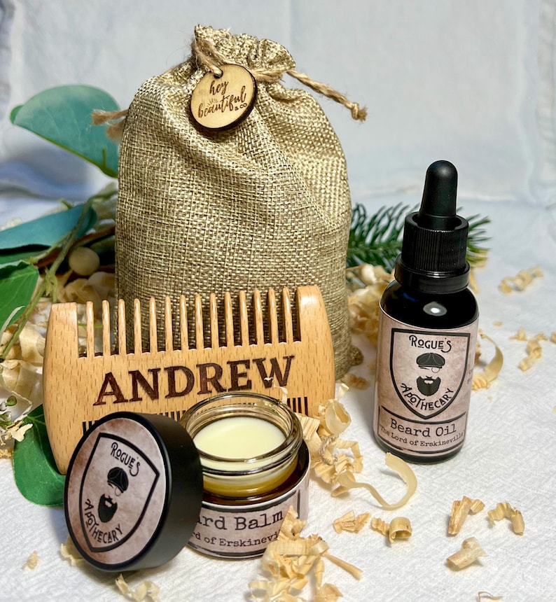 K&ouml;nnte beinhalten: Ein personalisierter Holzkamm mit dem eingravierten Namen "ANDREW", ein kleines Glas mit Bartbalsam, eine Flasche Bart&ouml;l und ein Jutesack mit einem Holzschild, auf dem "hey beautiful" steht.