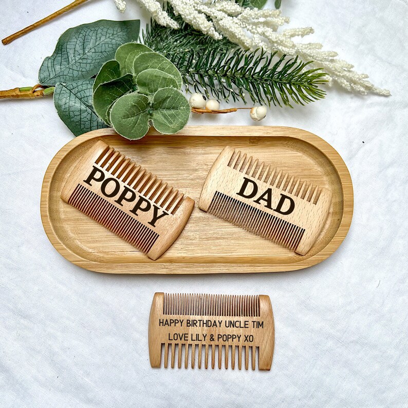 K&ouml;nnte beinhalten: Drei Holzk&auml;mme mit graviertem Text. Die K&auml;mme liegen auf einem Holztablett. Der Text auf den K&auml;mmen lautet "Poppy", "Dad" und "Happy Birthday Uncle Tim Love Lily & Poppy XO".