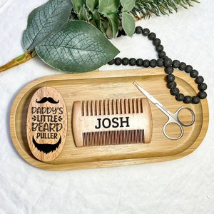 May include: A wooden tray with a beard comb, a small wooden brush with the text "Daddy's Little Beard Puller", and a pair of small scissors. The comb has the name "Josh" engraved on it.