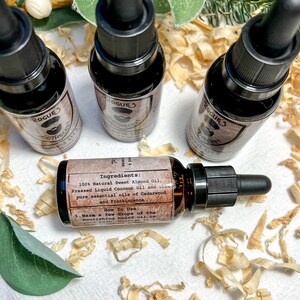 K&ouml;nnte beinhalten: Drei kleine braune Glasflaschen mit schwarzen Tropfern und Etiketten mit der Aufschrift "Rogue's Apothecary Beard Oil". Die Flaschen stehen auf einer Oberfl&auml;che, die mit Holzsp&auml;nen bedeckt ist. Das Etikett auf einer Flasche listet die Zutaten und Gebrauchsanweisungen auf.