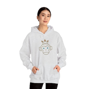 May include: A light gray hooded sweatshirt featuring a monkey face with a crown graphic. The monkey face is outlined in brown with blue eyes. The crown is brown with gold accents. The sweatshirt has a front pocket and a drawstring hood.