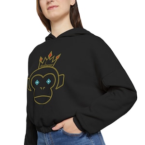 May include: Black cropped hoodie featuring a gold outline of a monkey wearing a crown, with the text "6ixSense" above the monkey. The monkey has turquoise eyes. The hoodie has a drawstring at the waist and a hood.