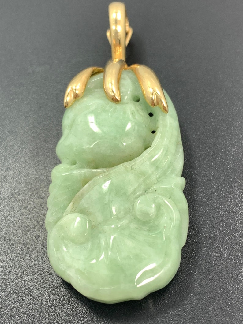 May include: A green jade pendant carved with a floral design, set in a gold pendant bail.