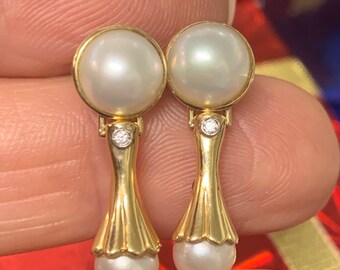 May include: A pair of gold drop earrings with a pearl and a small diamond accent. The pearls are white and the earrings have a delicate design.