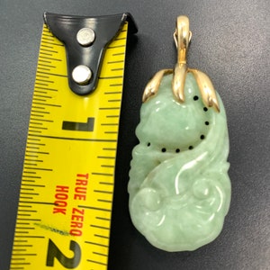 May include: A green jade pendant carved with a floral design, set in gold with a bail for a chain. The pendant is about 2 inches long.