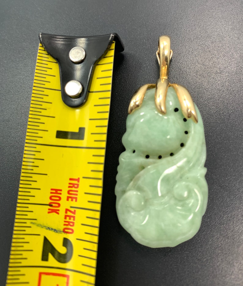 May include: A green jade pendant carved with a floral design, set in gold with a bail for a chain. The pendant is about 2 inches long.