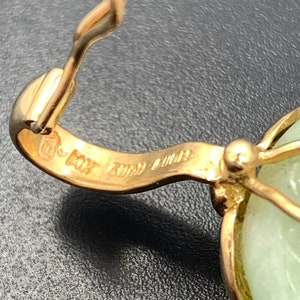 May include: Close-up of a gold pendant with a green jade stone. The pendant has a hallmark that reads "14K Italy 585".
