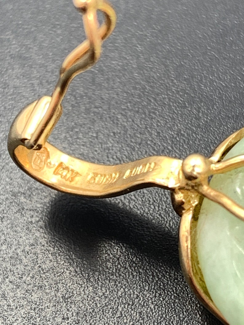 May include: Close-up of a gold pendant with a green jade stone. The pendant has a hallmark that reads "14K Italy 585".