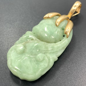 May include: A green jade pendant with a gold bail. The jade is carved in a floral design.