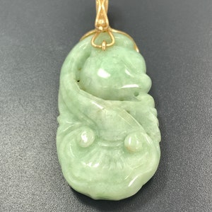 May include: A green jade pendant carved with a floral design, suspended from a gold chain.