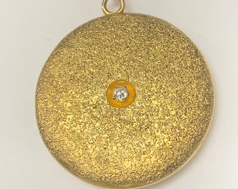 May include: A gold locket pendant with a textured surface and a small diamond in the center.