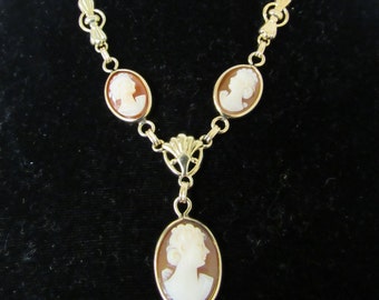 May include: A gold-toned necklace featuring four oval cameo pendants with white profile figures set against a brown background. The necklace has a delicate chain and decorative connectors, creating an elegant and classic jewelry piece.