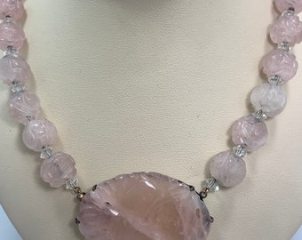 May include: A pink rose quartz necklace with a large carved rose quartz pendant. The necklace is made of faceted rose quartz beads and clear glass beads.