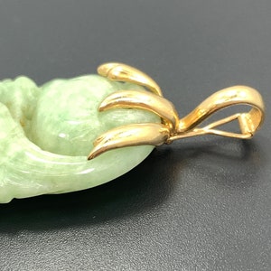 May include: A jade pendant with a gold bail. The jade is carved in the shape of a flower with a green hue.