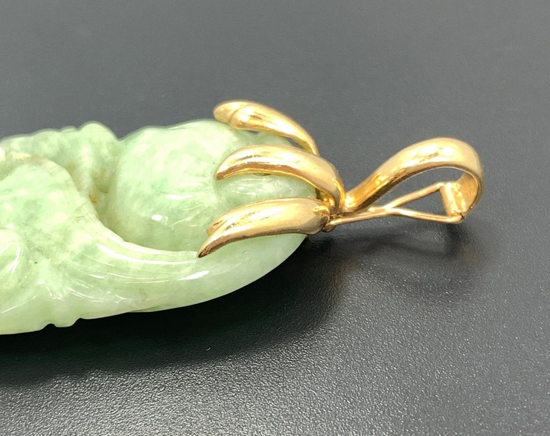 May include: A jade pendant with a gold bail. The jade is carved in the shape of a flower with a green hue.