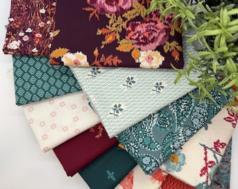 May include: A collection of fabric swatches in various patterns and colors. The fabrics include floral, geometric, and paisley designs in shades of burgundy, teal, cream, and green. A sprig of greenery is in the upper right corner.