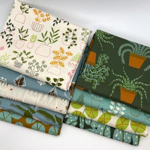 May include: A stack of fabric pieces with various plant and pot designs. The fabrics feature illustrations of potted plants in shades of green, orange, and pink on backgrounds of white, teal, and olive green. The fabrics are suitable for sewing and crafting projects.
