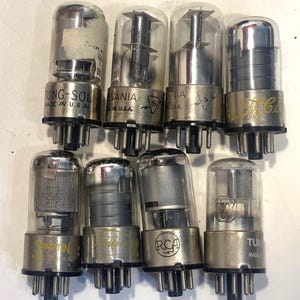 以下が含まれることがあります： ガラス製のエンクロージャーと金属製のベースを備えた、8つのヴィンテージ真空管のコレクション。Tung-Sol、Sylvania、RCAなどのブランド名が記されており、「Made in U.S.A.」の刻印があります。これらの電子部品は、オーディオアンプやその他の電子機器に使用されています。