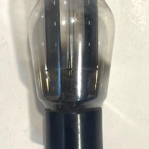 May include: A vintage vacuum tube with a clear glass bulb and a black base. Inside the glass, there are internal components and filaments. The tube has several pins extending from the base, designed for insertion into a socket.