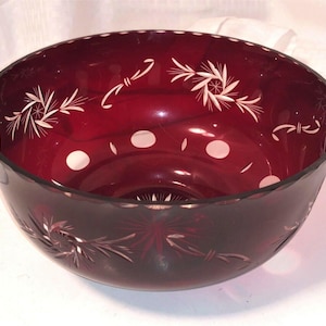 May include: A ruby red glass bowl with intricate white etched floral and dot patterns. The bowl has a wide, rounded shape with a slightly scalloped rim. The etched designs add a decorative touch to the bowl.