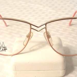 Puede incluir: Gafas con montura de metal dorado y detalles en rosa. Las lentes son transparentes y las monturas tienen una forma distintiva. La marca "DG-Line Robert" es visible en la lente izquierda.