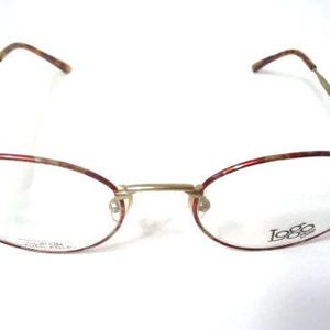 May include: Oval-shaped eyeglasses with a gold-colored frame and red and brown patterned rims. The temples are gold with brown tips. The lenses are clear, and the brand name "1986" is visible on the right lens.
